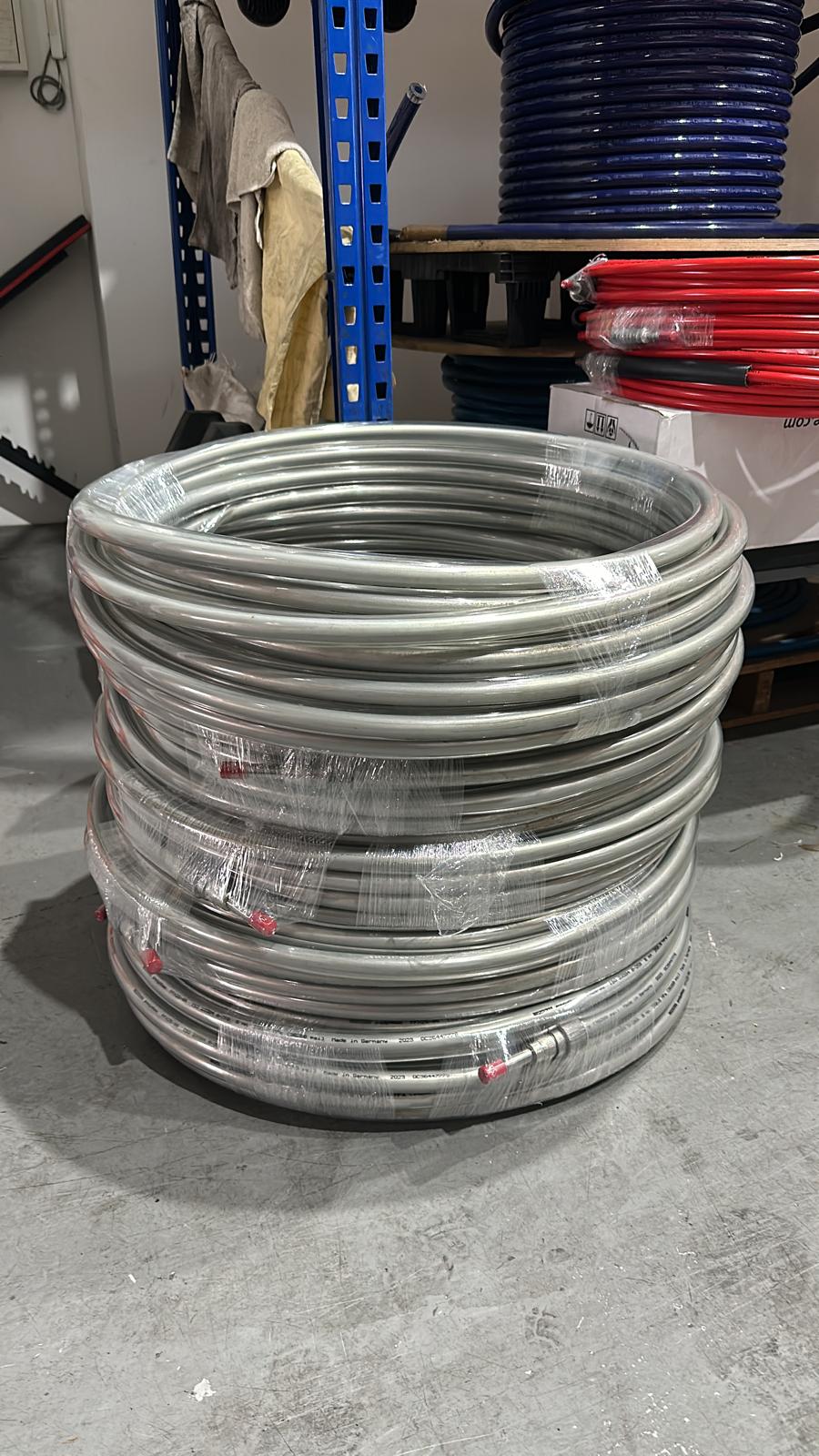Neatly stacked silver hoses in coils, stored in a warehouse or industrial setting with labels attached.