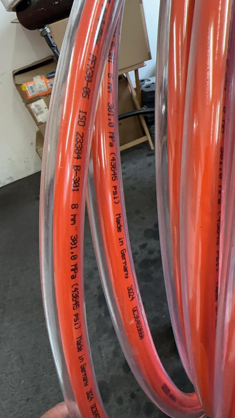 Bundle of bright orange hoses with labels, stored vertically in an industrial environment for easy access.
