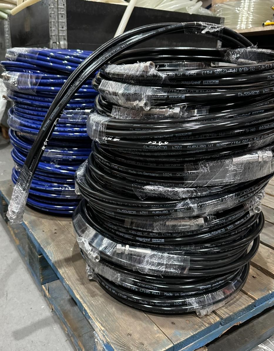 Stacked coils of black and blue hoses on a pallet, labeled and organized for industrial or construction use.
