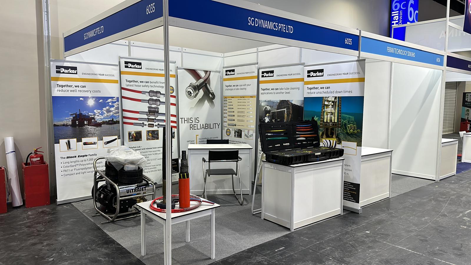 SG Dynamics booth with a table, chair, and equipment case, featuring posters and tools under booth number 625.