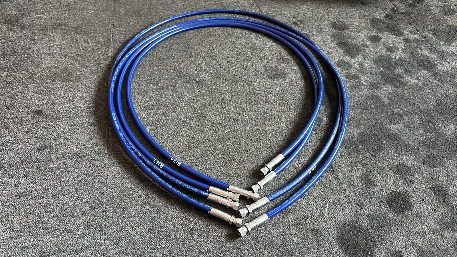 Coiled blue hydraulic hoses with metal fittings, neatly arranged on a concrete floor, ready for industrial use.
