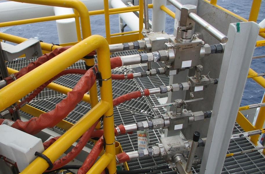 Yellow hoses secured along a metal railing, part of an industrial setup with valves and piping visible.